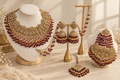 Filigree gold bridal jewellery set with ruby bead drops including collar necklace, jhumka earrings, passa side tikka and maang tikka displayed on white and gold stands